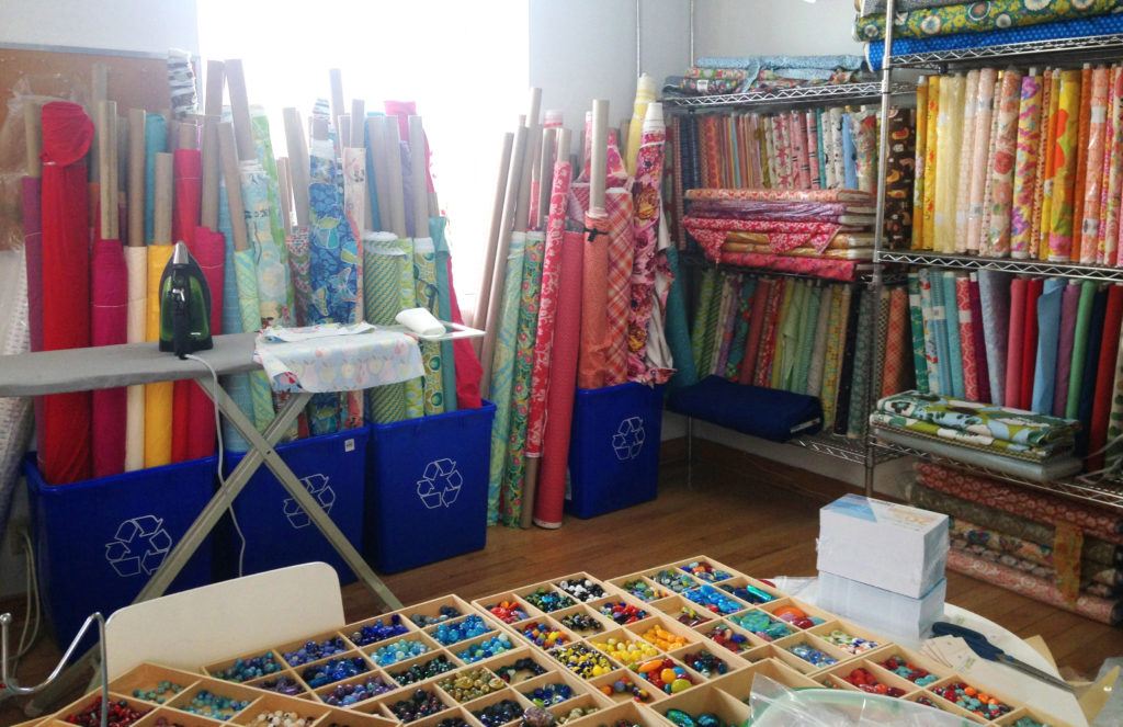 The fabric is all in one corner. I am still bringing fabric in and figuring out how best to organize it, but it's shaping up nicely. This photo was taken from Catherine's workspace, behind her bead/assembly table. The colour (of the glass and fabric together) is scrumptious.
